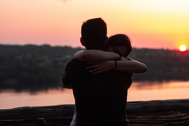 Mulher e homem brancos se abraçando no pôr do sol.