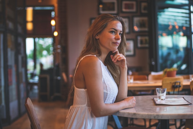 Mulher branca de cabelos loiros sentada num restaurante.