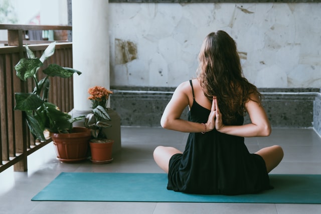 Mulher branca sentada num tapete de yoga, com os braços para trás.