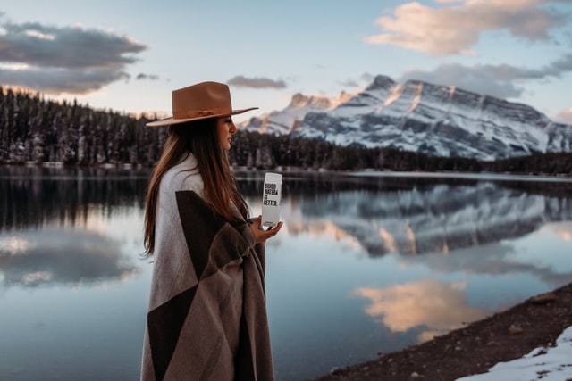 Mulher branca com roupas de inverno ao lado de lago.