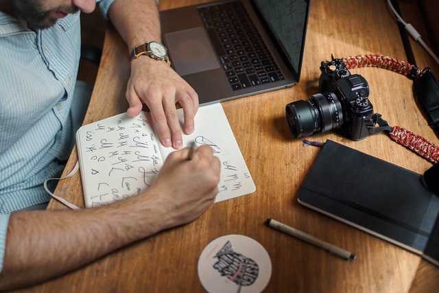 Homem branco desenhando num caderno.