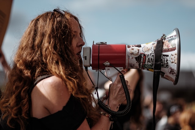 Mulher branca falando num megafone.