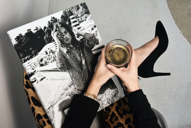 Mulher segurando revista e copo de café.