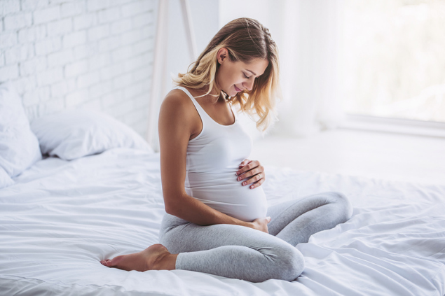 Gestante sentada na cama fazendo carinho na barriga