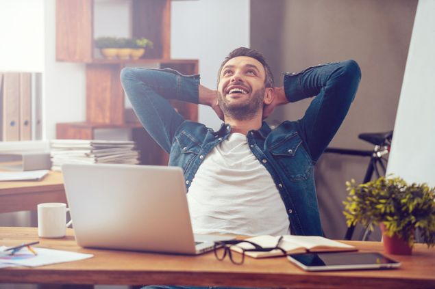 Homem feliz. Na frente dele, há uma escrivaninha com um computador
