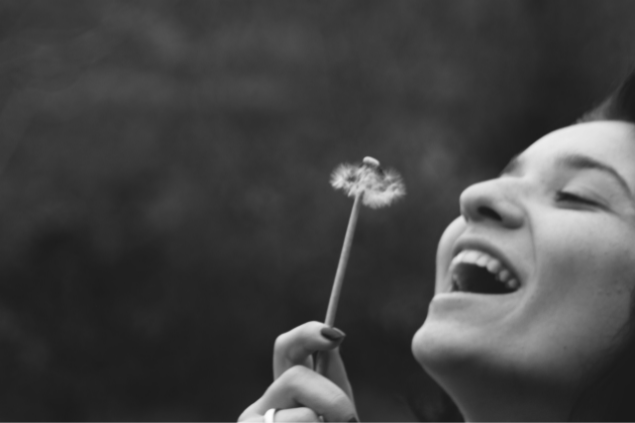 Mulher feliz assoprando um dente-de-leão