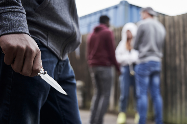 Homem se aproximando com uma faca perto de um grupo de adolescentes