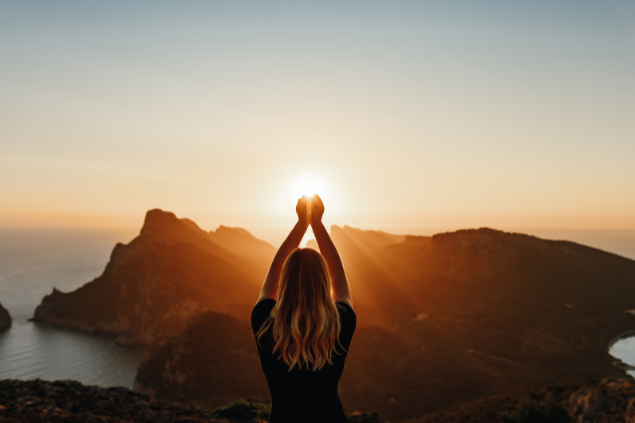 Mulher no topo de uma montanha com as mãos apontadas para o Sol