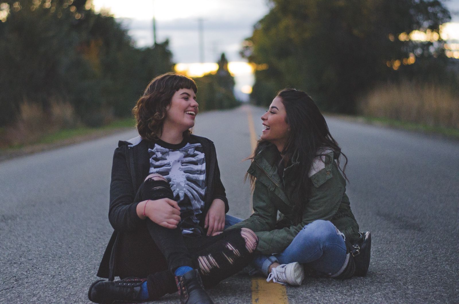 Mulheres brancas sentadas no asfalto sorrindo.