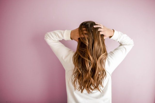 Mulher branca de costas com as mãos no cabelo.