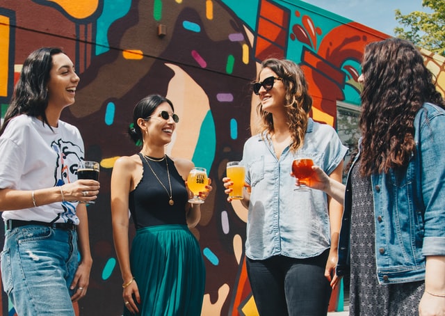 Mulheres brancas com copos na mão e sorrindo.