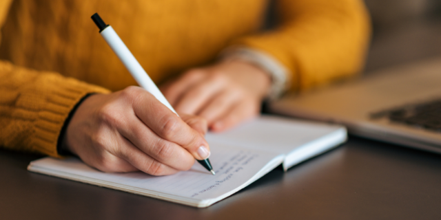 Mulher escreve em caderno. 