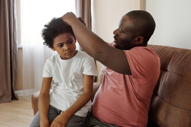 Pai arrumando o cabelo de sua filha, no sofá.