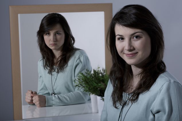 Imagem de uma mulher sorrindo e olhando para frente, mas seu reflexo no espelho mostra raiva.