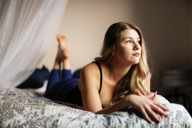 Mulher branca deitada numa cama.