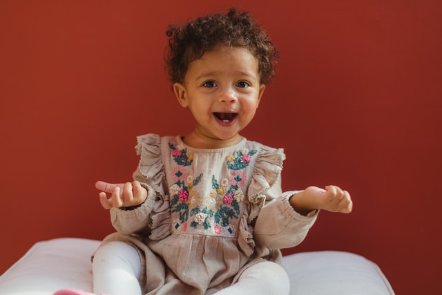 Bebê negra com os braços abertos e expressão sorridente.