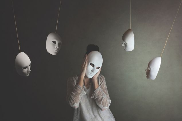 Mulher com uma máscara branca cobrindo o rosto. Outras máscaras estão penduradas ao seu redor.