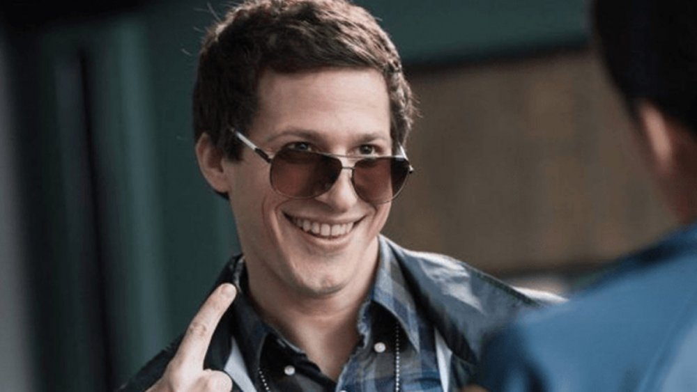 Homem branca com óculos de sol, apontando para si mesmo, com expressão sorridente.