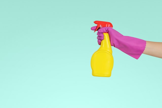 Mão com luva roxa segurando spray de embalagem amarela e tampa vermelha.