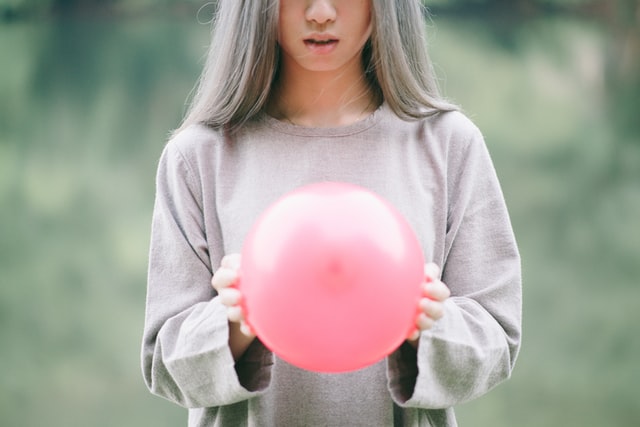 Mulher branca segurando balão rosa.