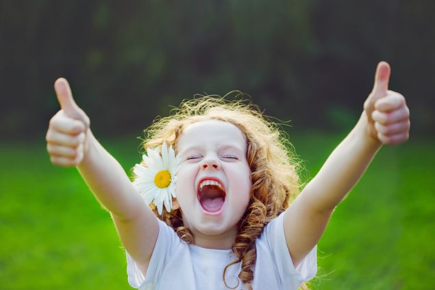 Garotinha muito feliz, fazendo sinal positivo com as mãos e com a boca aberta e olhos fechados como se estivesse gritando.