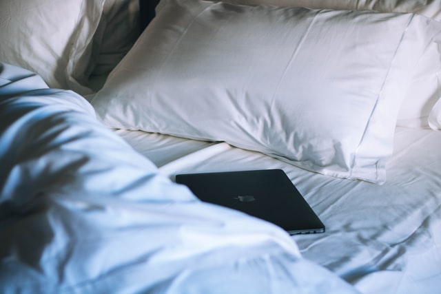 Cama branca com notebook preto fechado em cima.