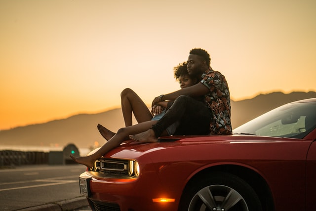Homem e mulher negros abraçados sentados em cima do carro.