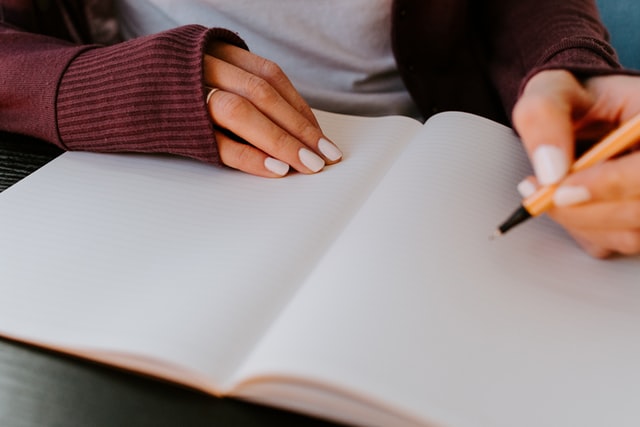 Mulher branca escrevendo num caderno.