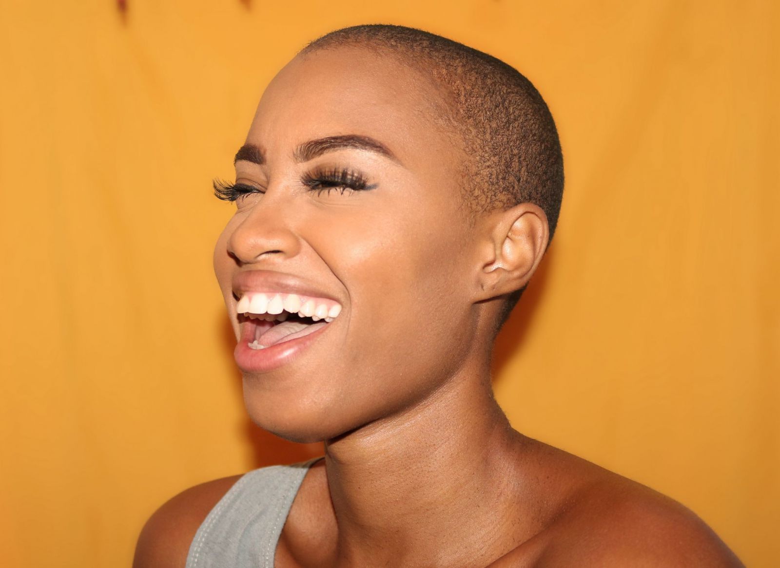 Mulher de cabelo raspado sorrindo vista de perfil.