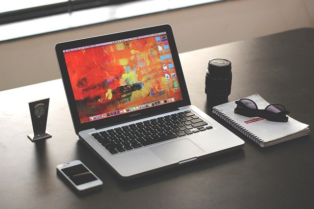 Mesa de trabalho organizada com notebook, celular, caderno, óculos de sol