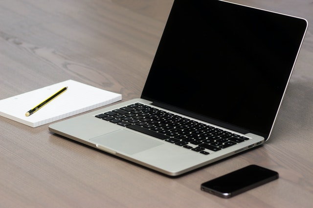 Mesa de trabalho com bloco de anotações, caneta, notebook e celular
