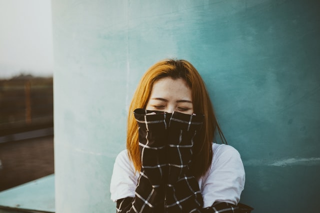 Mulher asiática com as mãos no rosto e olhos fechados.