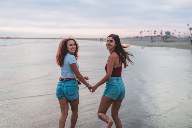 Mulheres brancas de mãos dadas na praia.
