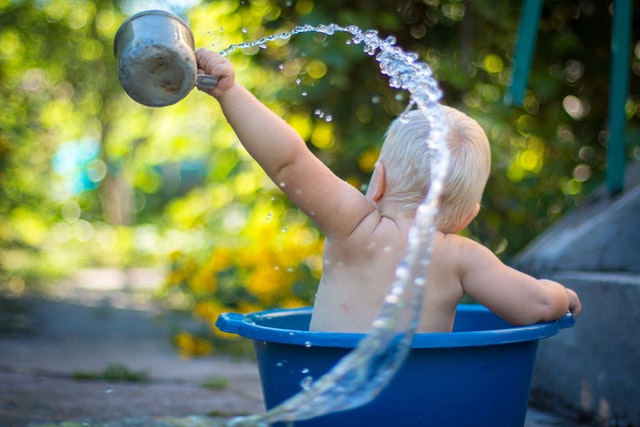 Bebê branco brincando numa bacia de água.