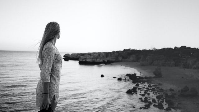 Mulher branca de lado numa praia.
