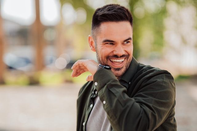 Homem branco sorrindo com a mão no rosto.