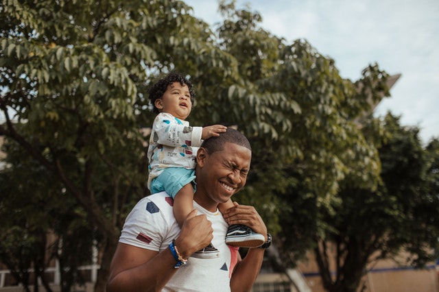 Pai com seu filho pequeno em seus ombros, sorrindo