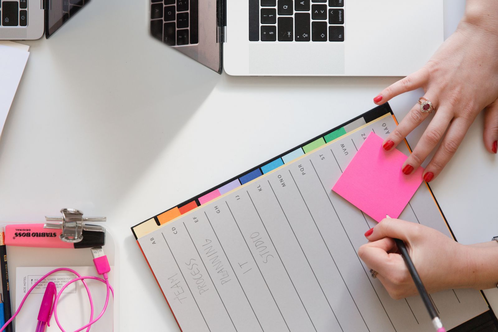 Mulher escrevendo em um post it ao lado de um notebook e um planeer