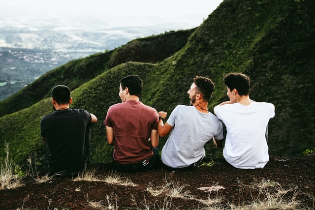 Quatro homens brancos sentados de costas num morro.