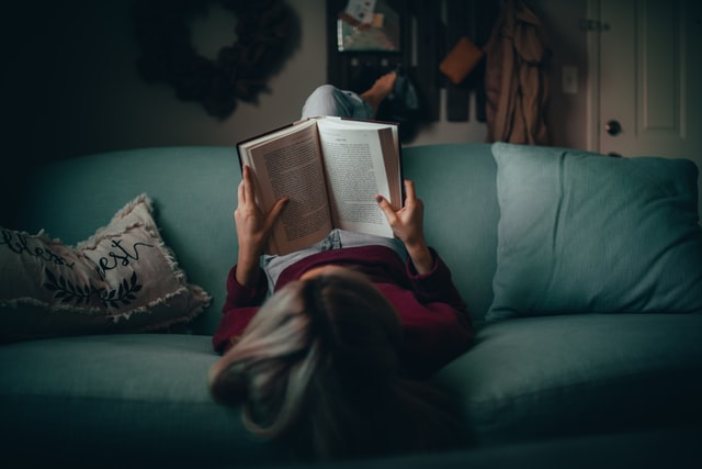 Mulher deitada de pés para cima numa sofá enquanto lê livro.