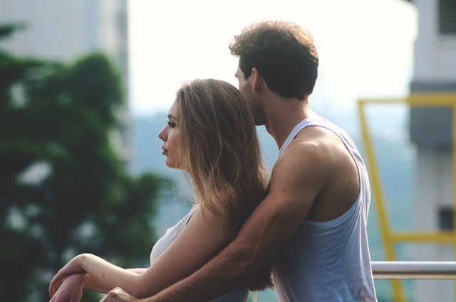 Homem branco abraçando mulher por trás.