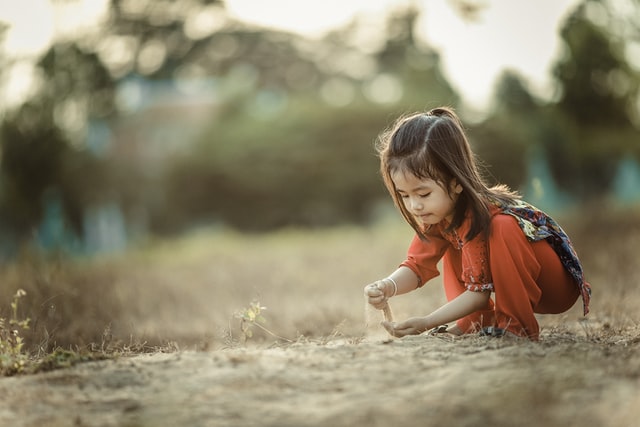Menina agachada brincando com areia