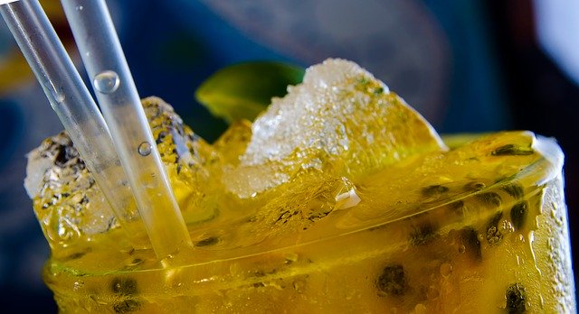 Copo transparente com líquido amarelo e cubos de gelo.