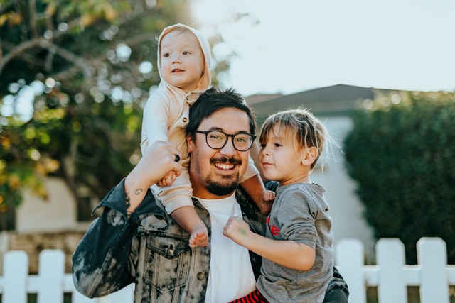 Homem com bebê nas costas e outro bebê no colo