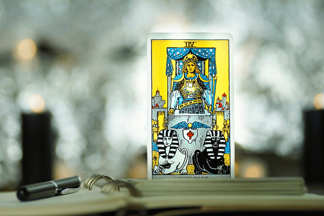 Na imagem, há a carta O Carro do Tarot na posição normal e em pé. Embaixo dela, há um caderno aberto e uma caneta.