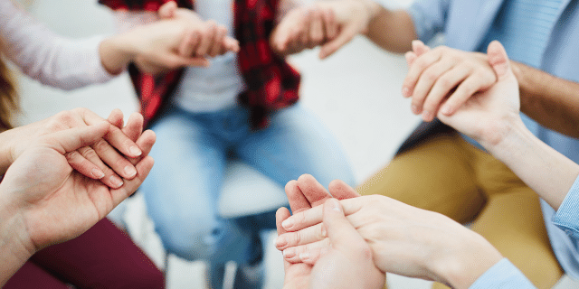 Recorte de várias pessoas em roda de mãos dadas rezando. 