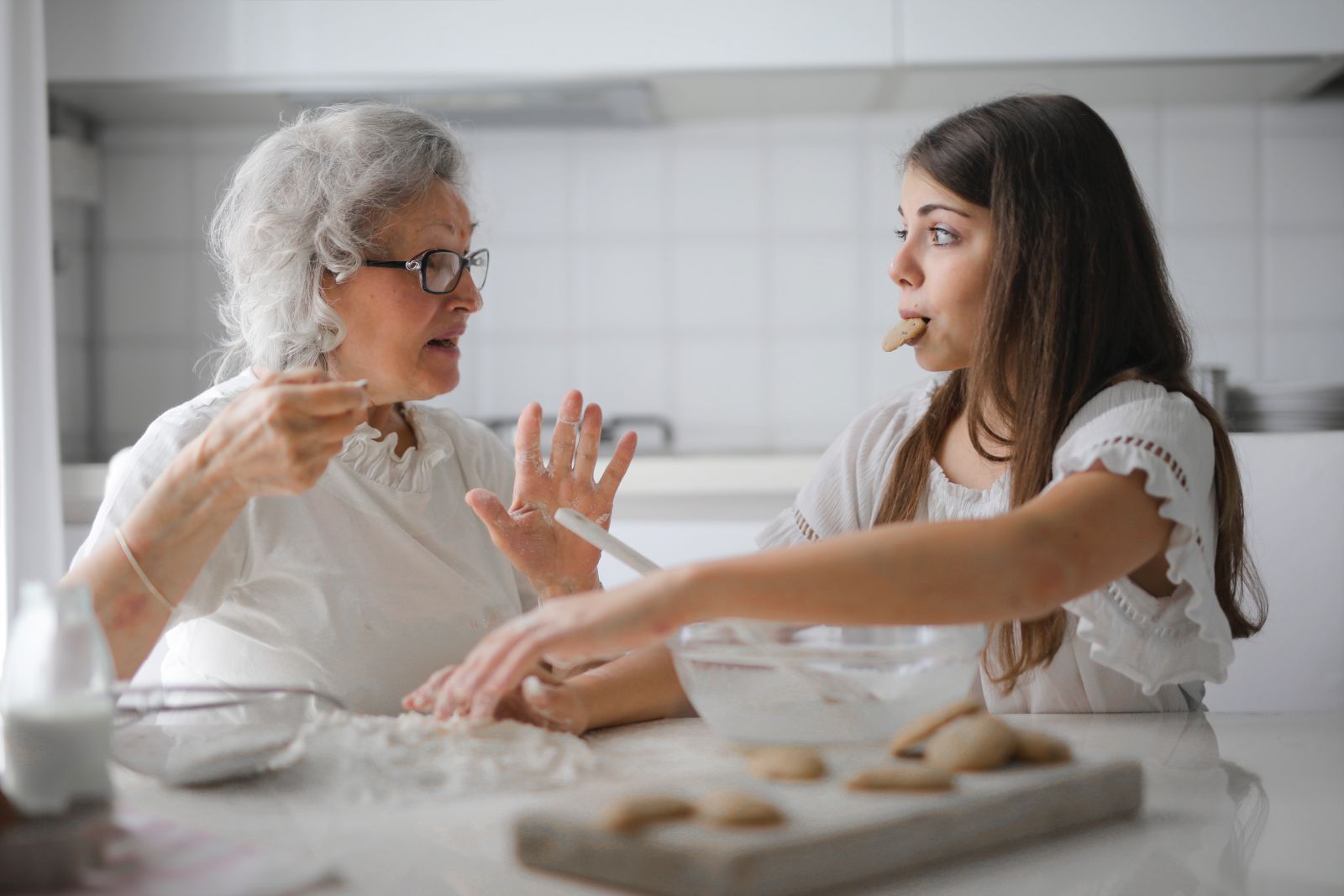 Avó cozinhando com sua neta, que rouba um biscoito.