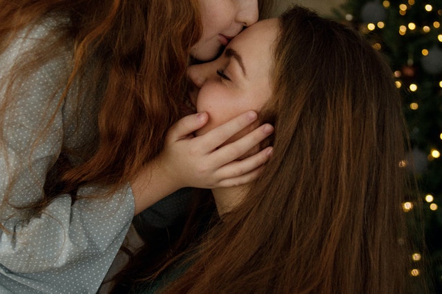 Criança branca beijando cabeça de mulher branca.