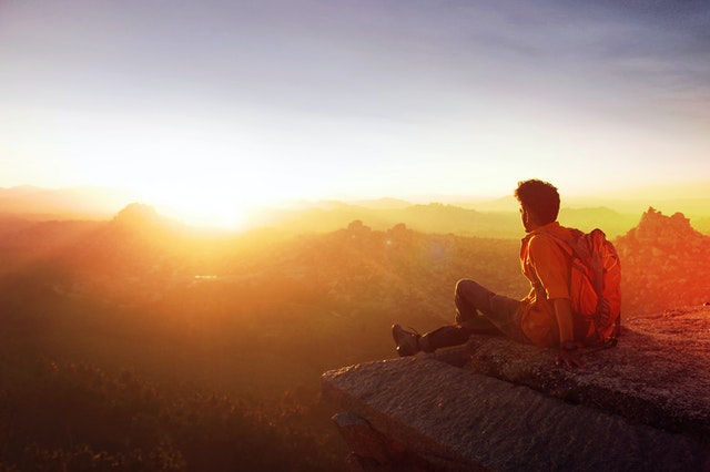 Homem sentado sob uma pedra olhando o pôr do sol