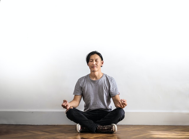 Homem sentado no chão, com as pernas cruzadas, meditando